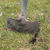 Spade pushed into the ground to make a slit perpendicular to another slit, forming a T shape